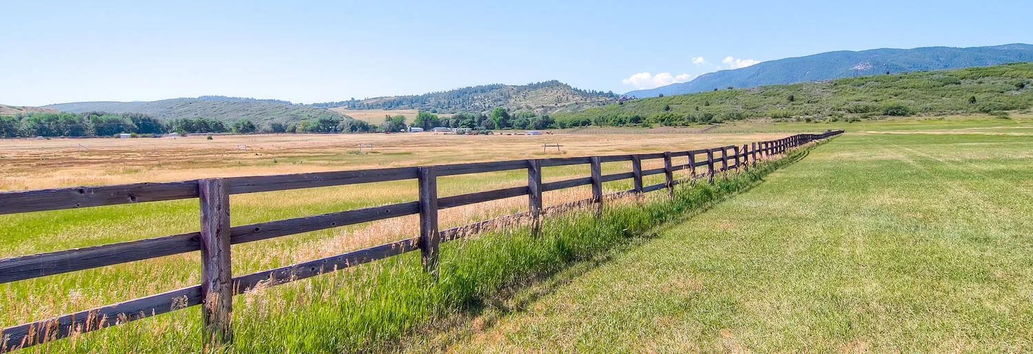 Wooden ranch fence along a green pasture with foothills behind